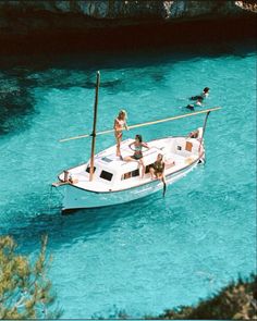 some people are on a small boat in the blue water and one person is swimming