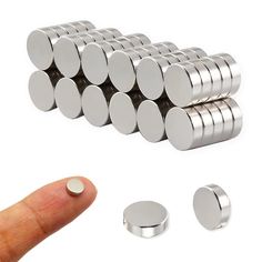 a finger is pointing at several magnets in the shape of round discs on a white background