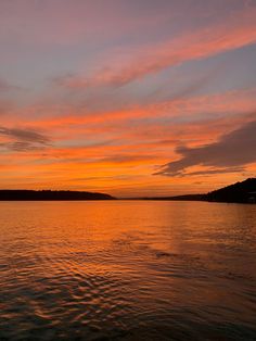 an orange and pink sunset over water with hills in the distance on either side, as seen from a boat