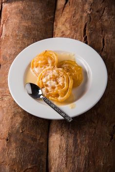 a white plate topped with food on top of a wooden table next to a spoon