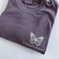 My absolute favorite tee! These butterfly tees can be customized to your preferred thread color and is stitched on a Comfort Colors short sleeve unisex tee. Each tee features a embroidered butterfly with 'transformed' below.  Please wash on gentle cycle and dry on low.  If you are wanting a different design, wording, or a different clothing style, please send me a message so we can discuss the details. Please include thread color at checkout If you need this order rushed, please add these to your cart: https://www.etsy.com/listing/1043569716/rush-my-order-for-t-shirts?ref=shop_home_active_19&frs=1 Rush my order + Priority shipping, click here: https://www.etsy.com/listing/1043567696/rush-my-order-priority-shipping-for-t?ref=shop_home_active_35&frs=1 Butterfly Tshirt, Spring Butterfly Embroidered Crew Neck T-shirt, Butterfly Christian Shirt, Blue Short Sleeve T-shirt With Butterfly Print, Casual T-shirt With Butterfly Print, Cute Spring Butterfly Print T-shirt, Embroidered Butterfly, Color Shorts, Short Sleeve Shirt