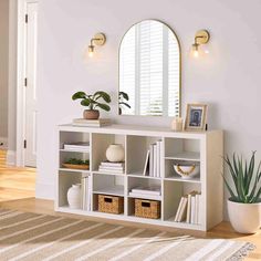 a white bookcase with books and plants on it in front of a round mirror