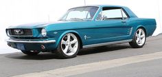 a blue mustang is parked in front of a white wall