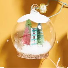 a glass ornament with a house and trees in it on a yellow background