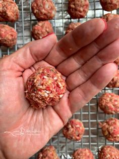 a hand holding a ball of meatballs on a wire rack with more meatballs in the background