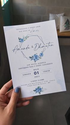 a person holding up a wedding card with blue flowers on the front and back side