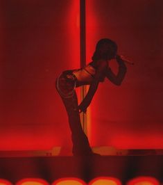 a woman standing on top of a stage next to a red wall with lights behind her