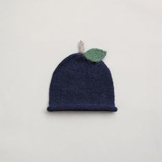 a blue knitted hat with a green leaf on the front and side, against a white background