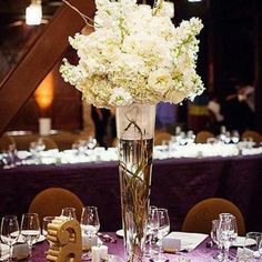 a tall vase filled with white flowers sitting on top of a purple table cloth covered table