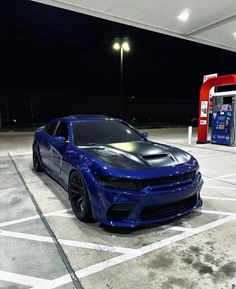 a blue car parked in a parking lot next to a gas pump at night time