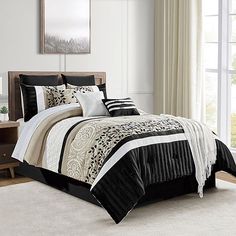 a bed with black and white comforters in a room next to a window on a rug