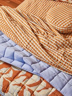 an orange and blue quilted bed spread on top of a wooden floor next to a pillow