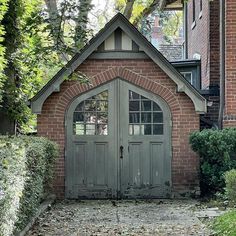 an old brick building with two double doors and arched windows on the front door is surrounded by greenery