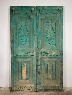 an old green door with ornate carvings on the front and side panels, in a white walled room