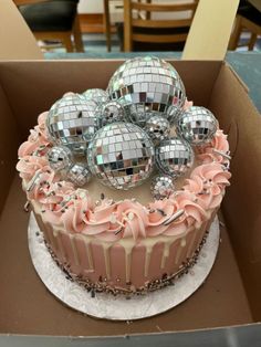 a cake with pink frosting and silver disco balls on top in a cardboard box