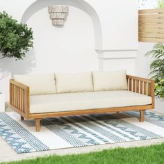 a wooden couch sitting on top of a rug next to a potted green plant