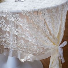 a white table cloth with lace and bows on it, sitting on top of a wooden floor