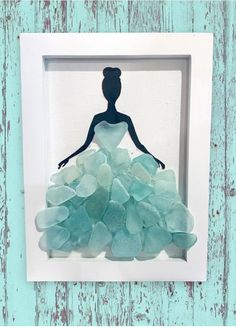 a shadow of a woman in a dress made out of sea glass on a white frame