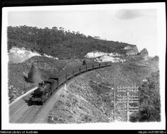 an old black and white photo of a train going down the tracks near a mountain