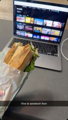 a person holding a sandwich in front of a laptop