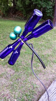 a blue dragonfly sculpture with three green balls on it's back legs and wings