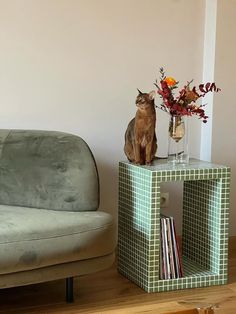 a cat sitting on top of a table next to a couch and vase with flowers