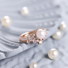 a close up of a pearl and diamond ring on a satin material with pearls around it