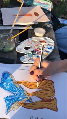 a person is painting on paper with paintbrushes and watercolors in front of them