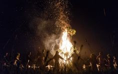 people standing around a bonfire at night with their arms in the air and fireworks coming out