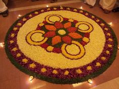 a flower arrangement on the floor with candles around it and people standing in the background