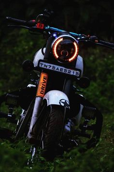 a close up of a motorcycle parked in the grass with its lights on at night