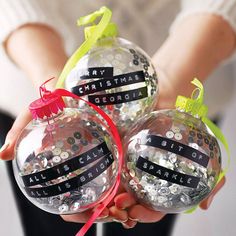 two christmas baubles with ribbons on them are being held by someone's hands