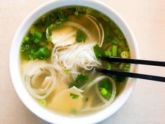 a white bowl filled with soup and veggies next to chopsticks on a table