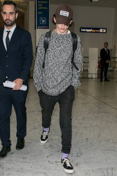 two men in suits are walking through an airport with one carrying a backpack and the other wearing a hat