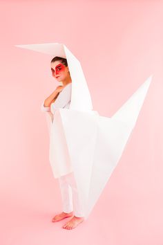 a woman with red eyeliners standing in front of a white paper bird on a pink background