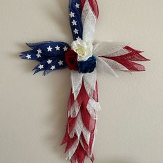 a cross made out of red, white and blue ribbon with flowers on it hanging from the wall