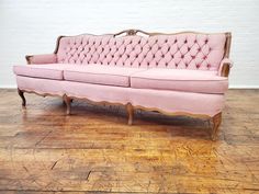 a pink couch sitting on top of a wooden floor next to a white brick wall