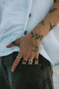 a person with tattoos on their arms and hand is holding onto his jeans pocket while wearing a white shirt