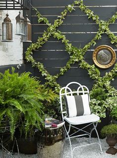 a white chair sitting in front of a black wall covered in plants and potted plants