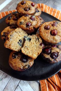 a black plate topped with muffins on top of a wooden table next to an orange and white towel