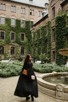 a woman walking in front of a building with ivy growing on it's walls