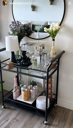 a bar cart with bottles and glasses on it in front of a wall mounted mirror