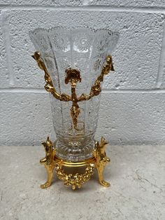 an ornate glass vase with gold decorations on the bottom and sides, against a white brick wall