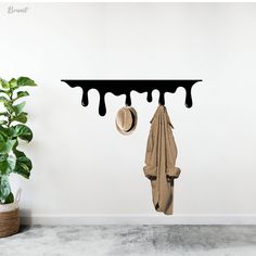 a white wall with a coat and hat hanging from it's hooks next to a potted plant