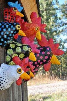 several colorful roosters are hanging on the side of a wooden pole in front of some trees