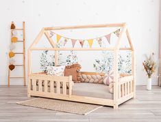 a child's wooden bed with a canopy and pillows on the bottom, in front of a wall decorated with bunting flags