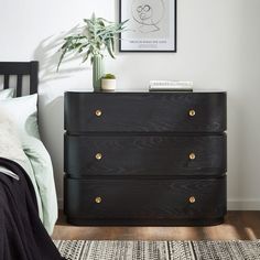 a bedroom with a black dresser next to a bed and a plant on top of it