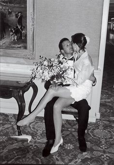 a man kissing a woman on the cheek in front of a chair with flowers behind her