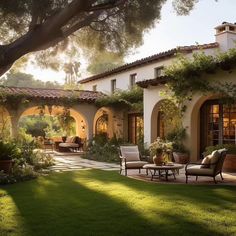 an outdoor patio with chairs and tables in front of a large house that is surrounded by greenery