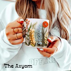 a woman is holding a coffee mug with flowers on it and the words, the axym